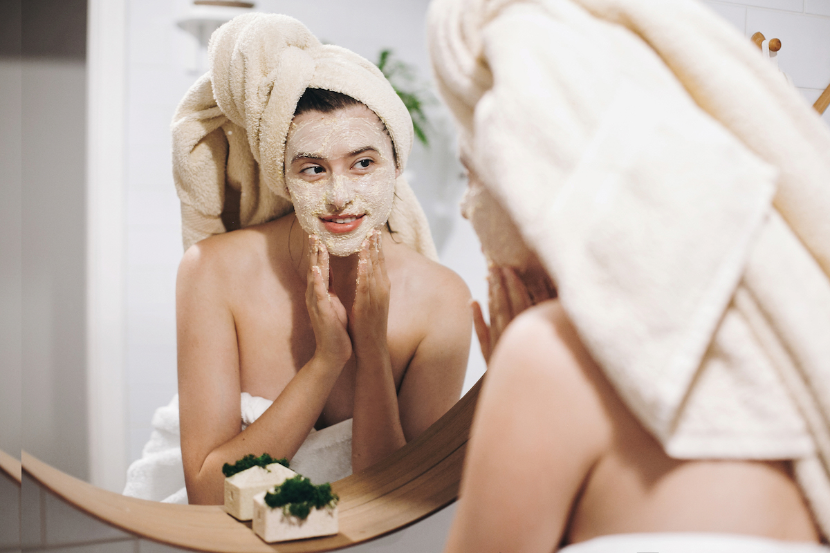 Young happy woman in towel making facial massage with organic face scrub