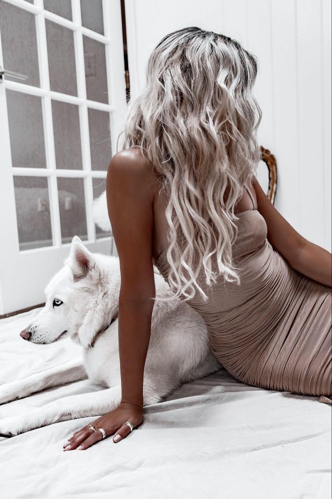Woman in taupe dress sits with white huskey