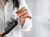 woman losing hair on hairbrush in hand on bathroom background, soft focus