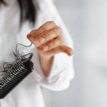 woman losing hair on hairbrush in hand on bathroom background, soft focus