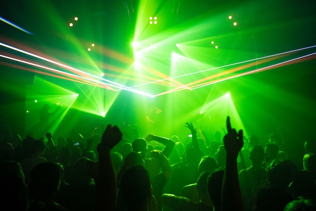 Des gens dansent dans un club pendant qu'un DJ joue de la musique électronique avec des lasers